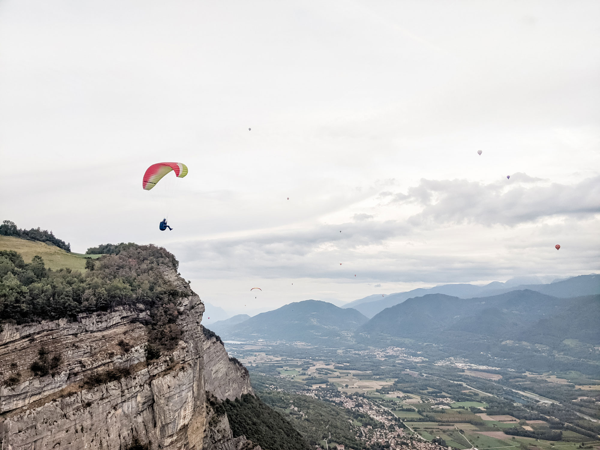woman paragliding off a mountain, hills in background