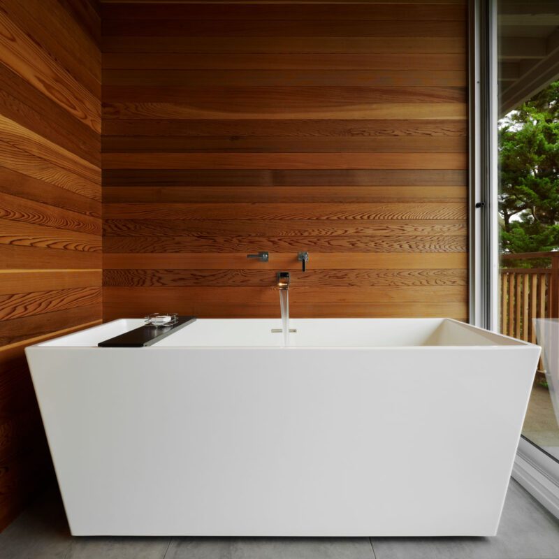 White freestanding bathtub with wooden walls with glass doors and deck access