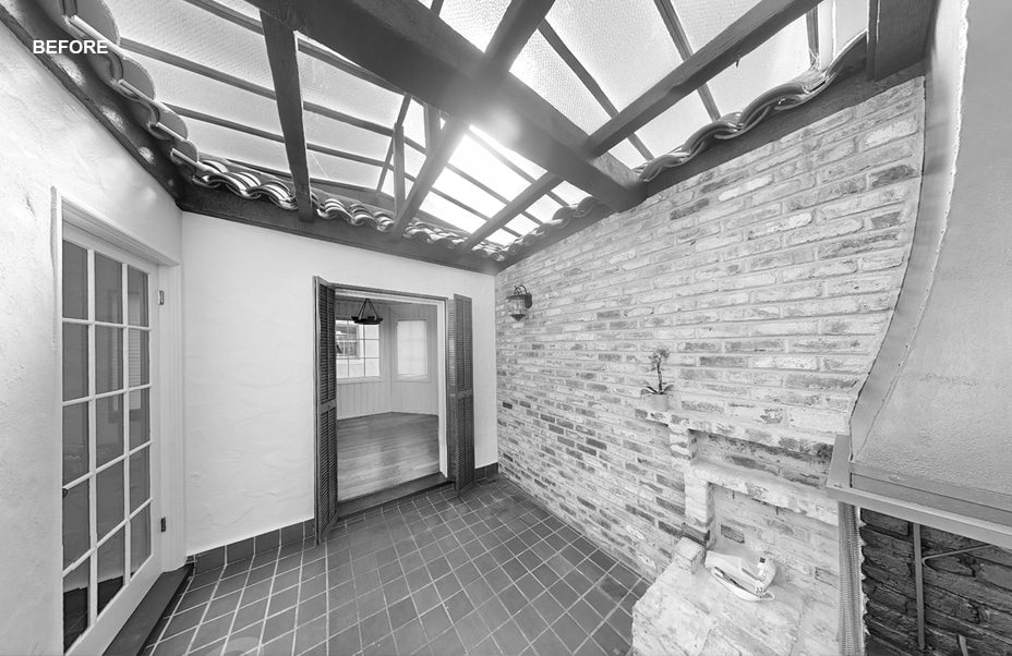 A sunroom with a glass ceiling, brick walls, tiled floor, and a small fireplace. French doors lead to another room. The word “BEFORE” appears in the upper left corner. The image is in black and white.