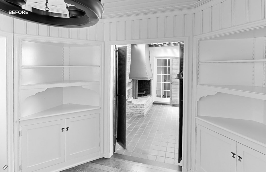 Black and white photo of an empty room with built-in shelves and cabinets, double doors open to a tiled patio with a brick fireplace. The word BEFORE appears in the upper left corner.
