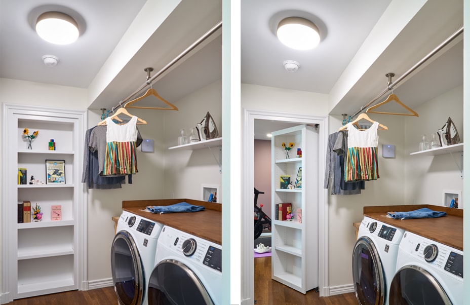A laundry room with a washer and dryer, shelves with books and decor, and a hanging rod with clothes. The right side shows a hidden door in the shelving unit partially open, revealing another room.